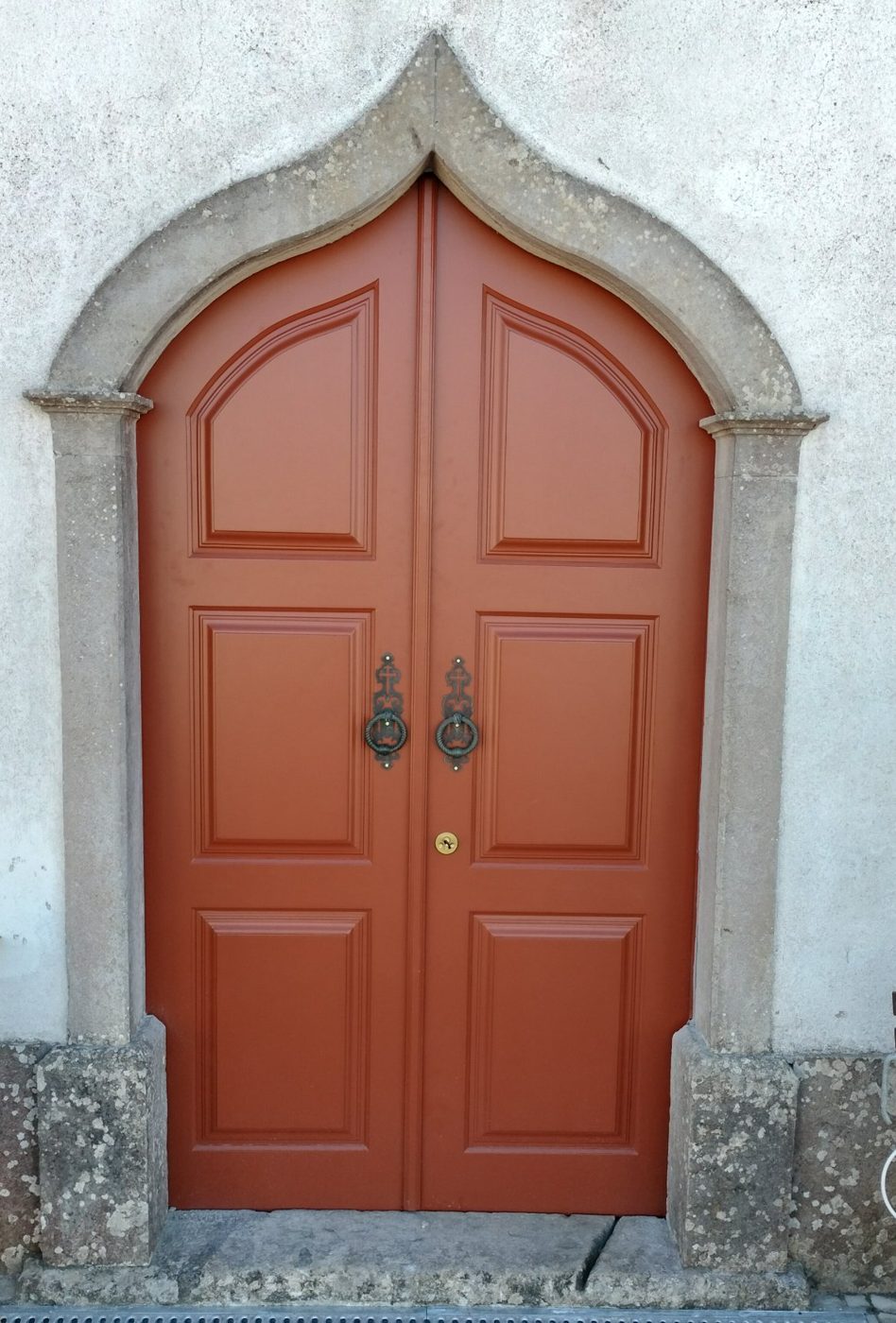 Porta de duas folhas em madeira, com almofadas e remate em arco, numa fachada antiga