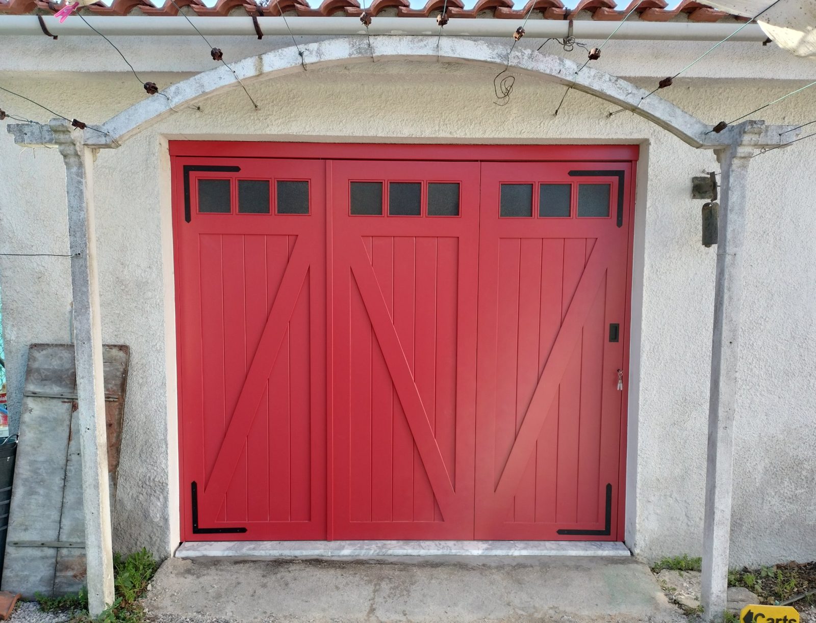 Portão de garagem em madeira, vermelho, com três folhas e postigos de vidro